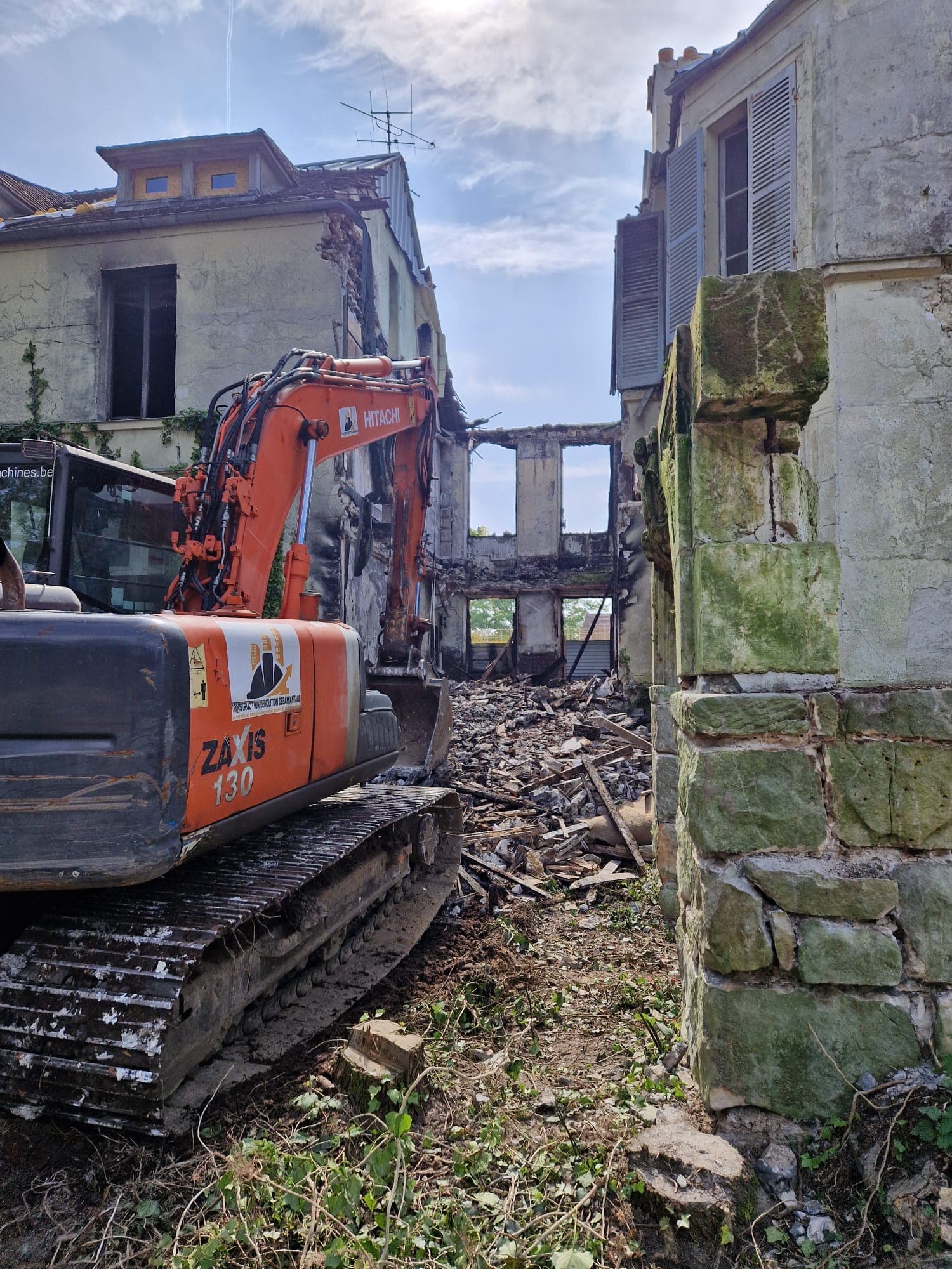 Pelle Hitachi de CDD devant un vieux bâtiment en pierre en cours de démolition