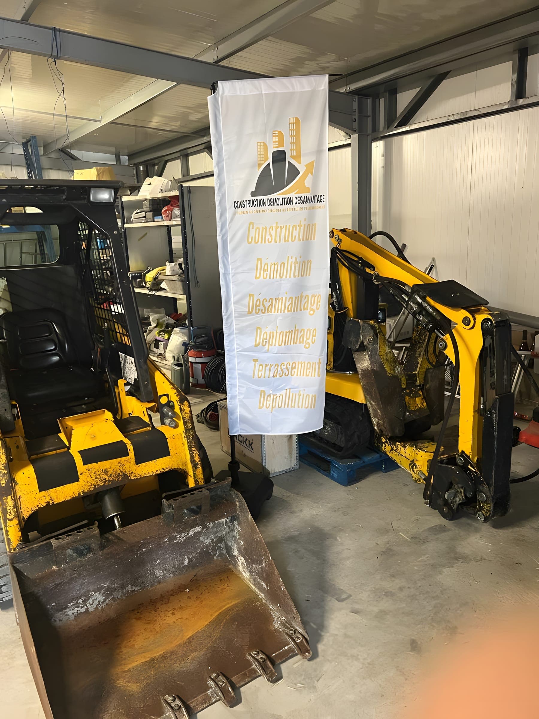 Robot de démolition Brokk dans l'atelier CDD, devant une bannière aux couleurs de l'entreprise